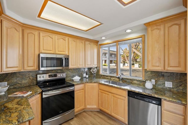 kitchen featuring sink, stainless steel appliances, dark stone countertops, and light brown cabinetry