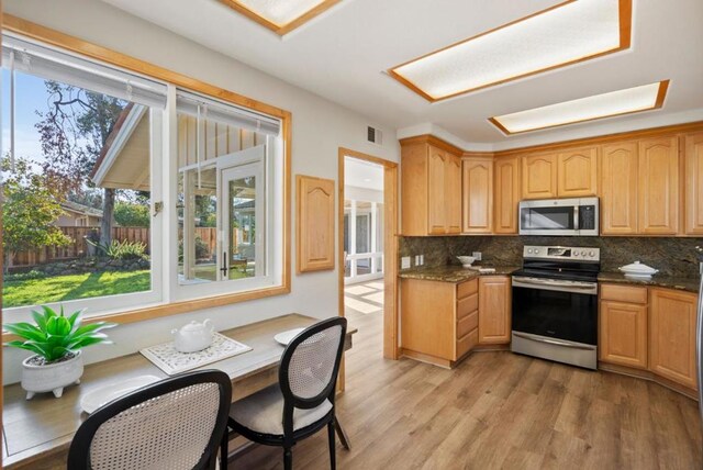 kitchen featuring stainless steel appliances, dark stone countertops, light hardwood / wood-style flooring, and decorative backsplash