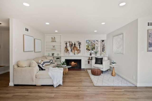 living room featuring light hardwood / wood-style floors, built in features, and a fireplace