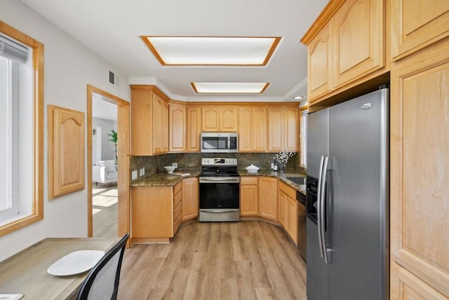 kitchen featuring light brown cabinets, stainless steel appliances, dark stone countertops, backsplash, and light wood-type flooring