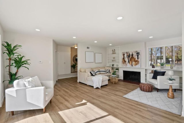 living room with built in shelves, light hardwood / wood-style floors, and a brick fireplace