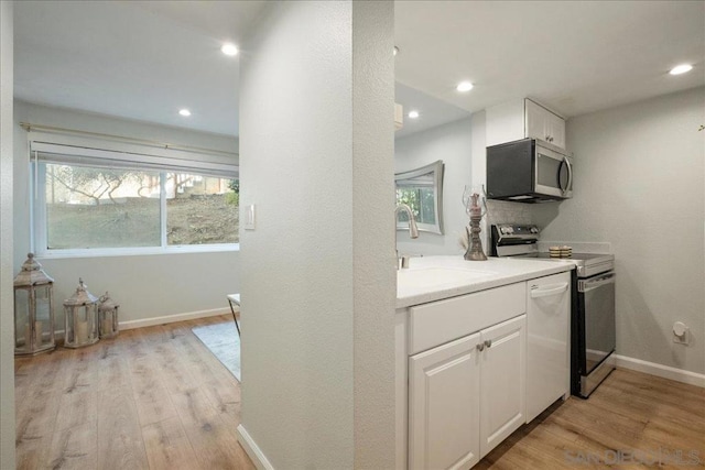 kitchen with appliances with stainless steel finishes, plenty of natural light, white cabinets, and light hardwood / wood-style floors