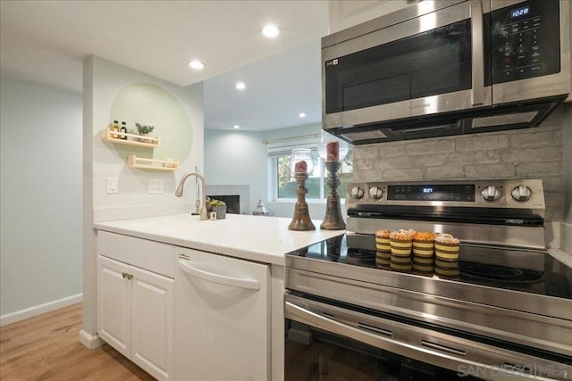 kitchen featuring appliances with stainless steel finishes, tasteful backsplash, white cabinetry, sink, and light wood-type flooring