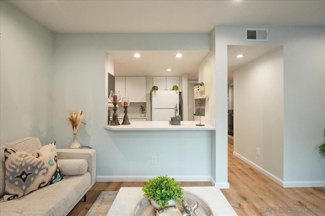 interior space featuring light hardwood / wood-style floors, kitchen peninsula, white cabinets, and white fridge