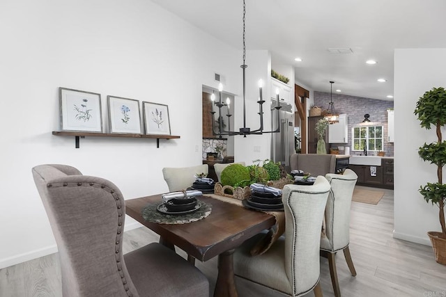 dining space featuring light wood-type flooring, brick wall, vaulted ceiling, and sink