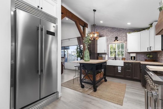 kitchen with vaulted ceiling, sink, built in fridge, and white cabinetry