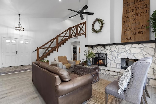 living room with high vaulted ceiling, ceiling fan, light hardwood / wood-style flooring, and a stone fireplace