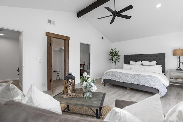 bedroom featuring ceiling fan, a closet, a walk in closet, light hardwood / wood-style flooring, and beamed ceiling