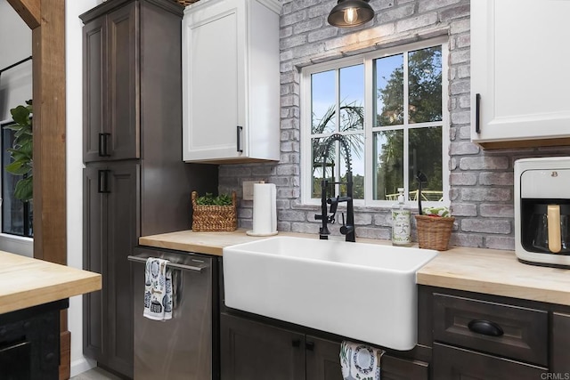 kitchen with wood counters, dishwasher, white cabinets, and sink