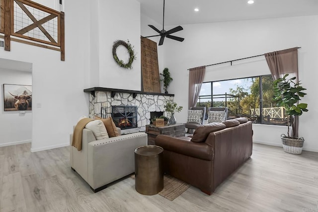 living room with ceiling fan, light hardwood / wood-style floors, a fireplace, and high vaulted ceiling