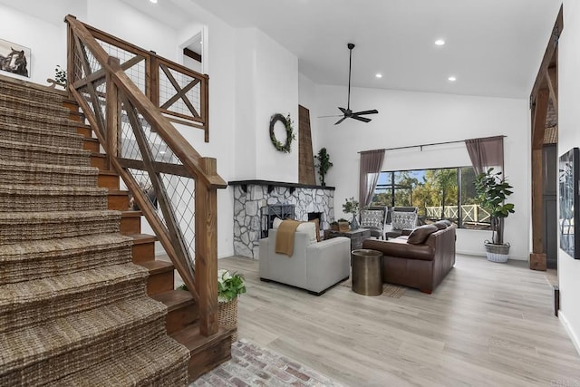 living room with ceiling fan, light hardwood / wood-style floors, a high ceiling, and a stone fireplace