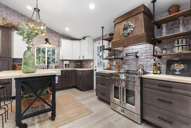 kitchen featuring white cabinets, dark brown cabinetry, lofted ceiling, hanging light fixtures, and high end stainless steel range oven