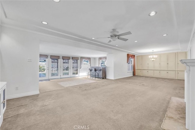 unfurnished living room featuring crown molding, ceiling fan with notable chandelier, and light colored carpet