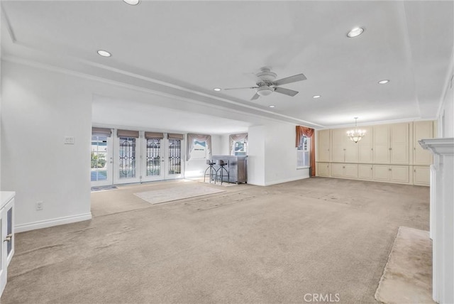 unfurnished living room featuring baseboards, light colored carpet, ornamental molding, and ceiling fan with notable chandelier