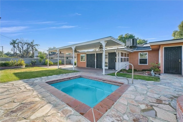 rear view of property featuring a patio, central AC unit, fence, a yard, and stucco siding