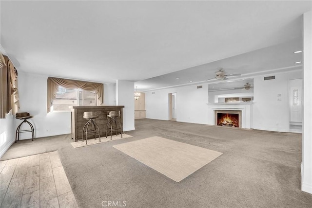 unfurnished living room featuring visible vents, ceiling fan, baseboards, carpet, and a lit fireplace