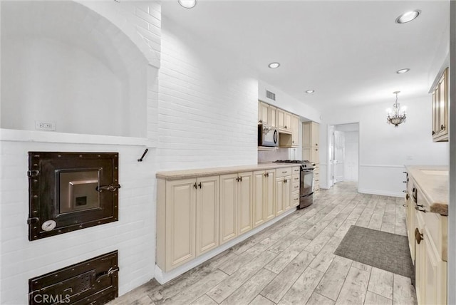 kitchen featuring pendant lighting, an inviting chandelier, cream cabinets, gas stove, and light wood-type flooring