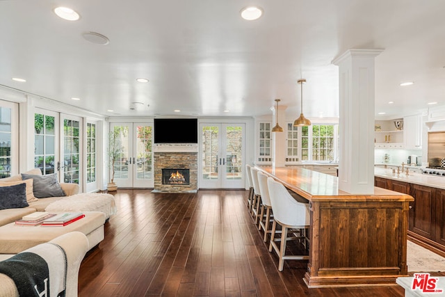 living room with dark wood-type flooring, french doors, a stone fireplace, and sink