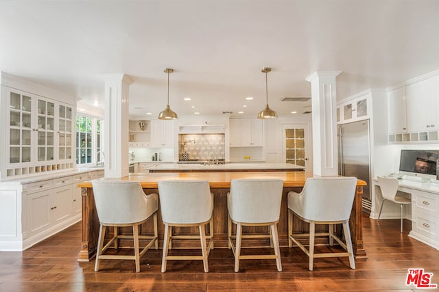 kitchen with a center island, a kitchen bar, white cabinets, butcher block counters, and built in fridge