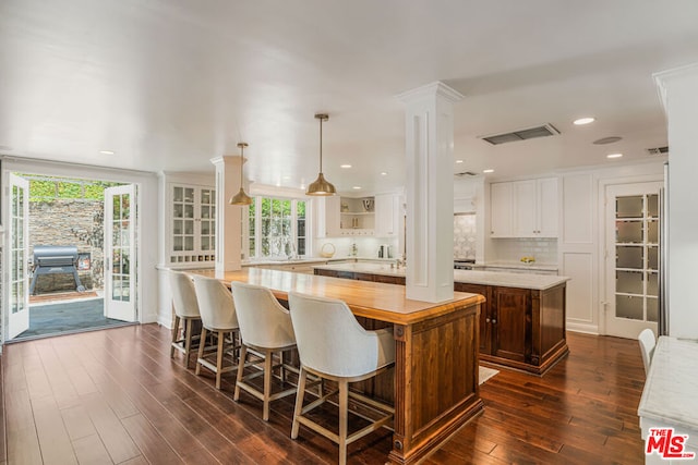 kitchen with kitchen peninsula, backsplash, a kitchen breakfast bar, dark wood-type flooring, and pendant lighting