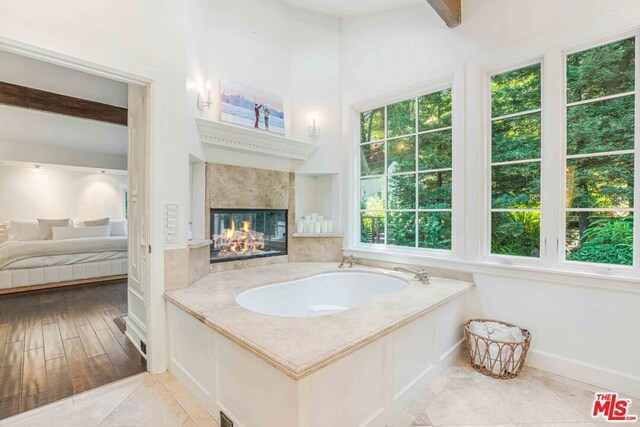 bathroom with a premium fireplace, tile patterned floors, beam ceiling, and a bathing tub