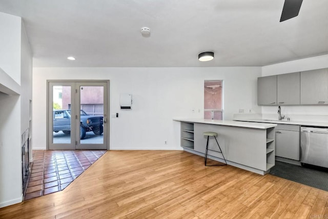 kitchen featuring kitchen peninsula, gray cabinets, dishwasher, a breakfast bar, and sink