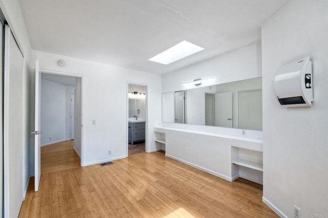 unfurnished bedroom featuring a skylight, light hardwood / wood-style floors, connected bathroom, and sink