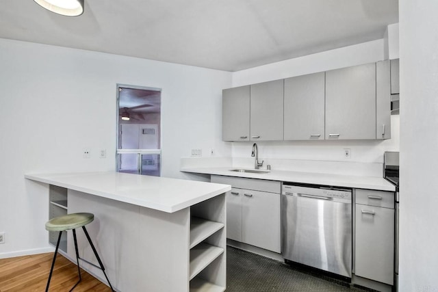 kitchen featuring kitchen peninsula, gray cabinets, dishwasher, a breakfast bar, and sink