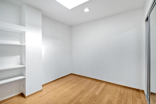 unfurnished room with built in shelves and light hardwood / wood-style flooring