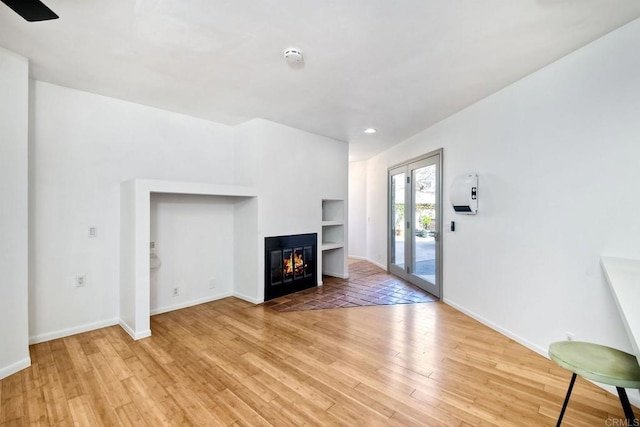 unfurnished living room featuring a multi sided fireplace, wood-type flooring, and built in features