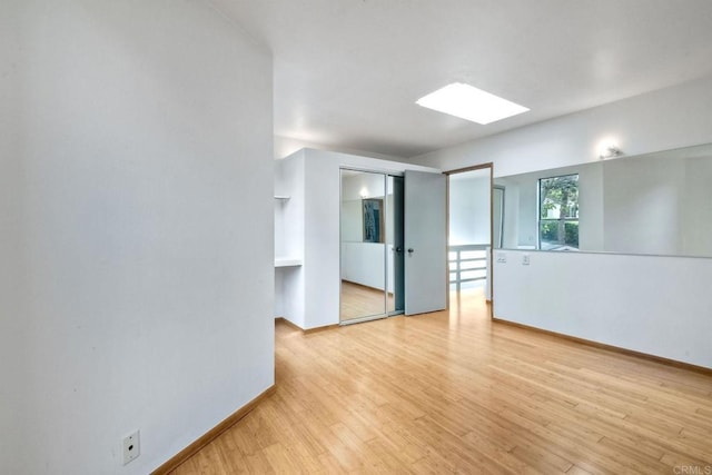 unfurnished room featuring a skylight and light hardwood / wood-style floors