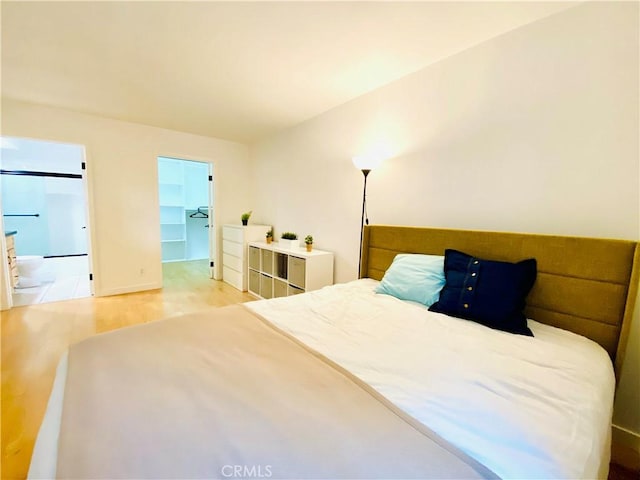 bedroom with a walk in closet, a closet, connected bathroom, and light hardwood / wood-style flooring