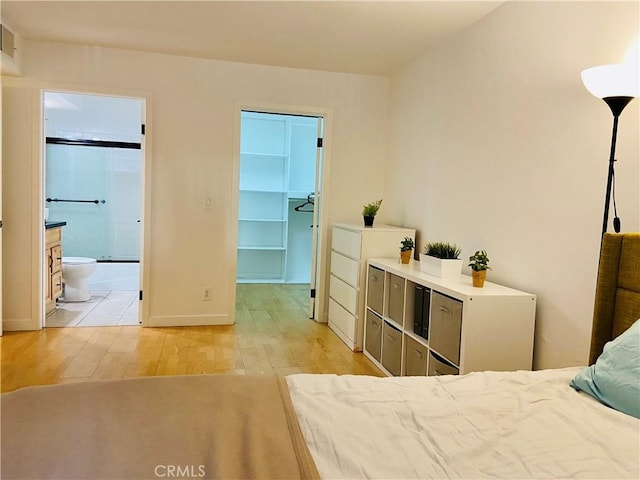 bedroom featuring ensuite bath, a walk in closet, a closet, and light hardwood / wood-style floors