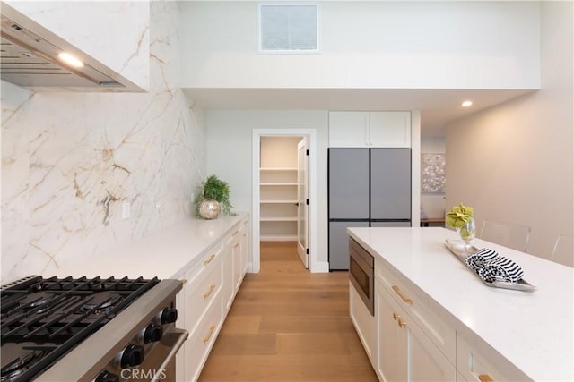 kitchen with decorative backsplash, wall chimney exhaust hood, white cabinetry, and light hardwood / wood-style flooring