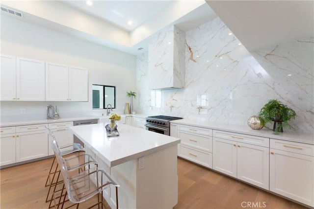 kitchen featuring a kitchen island, white cabinetry, light wood-type flooring, a breakfast bar area, and high end stainless steel range