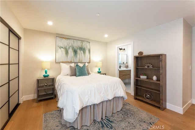 bedroom featuring connected bathroom and light hardwood / wood-style flooring