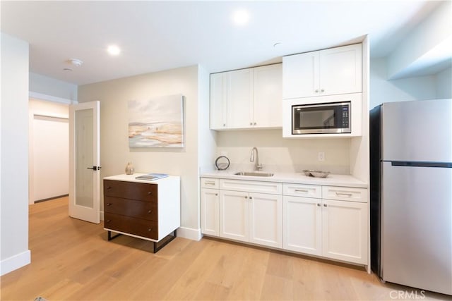 kitchen with appliances with stainless steel finishes, sink, white cabinetry, and light hardwood / wood-style floors