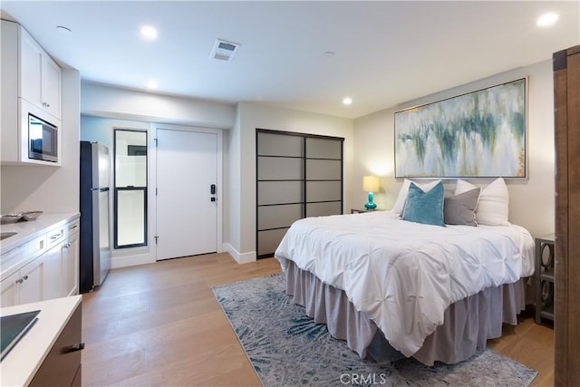 bedroom with light wood-type flooring and stainless steel refrigerator