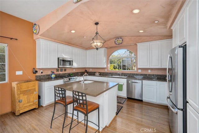 kitchen with a center island with sink, light hardwood / wood-style floors, pendant lighting, appliances with stainless steel finishes, and white cabinets