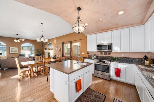 kitchen with white cabinetry, an island with sink, appliances with stainless steel finishes, pendant lighting, and ceiling fan with notable chandelier