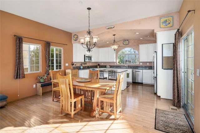 dining area featuring vaulted ceiling, a wealth of natural light, light hardwood / wood-style flooring, and a notable chandelier