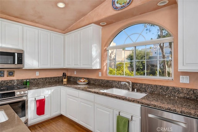 kitchen with vaulted ceiling, dark stone countertops, sink, white cabinetry, and appliances with stainless steel finishes