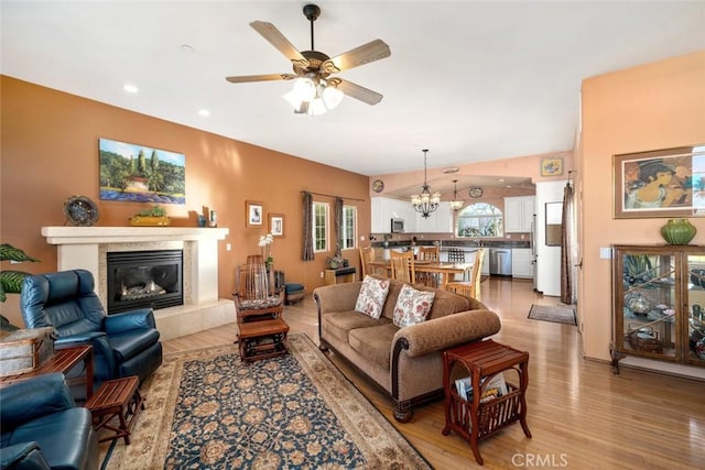 living room with ceiling fan with notable chandelier, hardwood / wood-style floors, and a tile fireplace