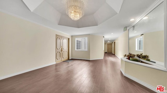 spare room with crown molding, hardwood / wood-style floors, an inviting chandelier, and a raised ceiling