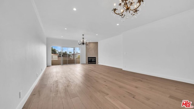 unfurnished living room with a large fireplace, light hardwood / wood-style flooring, an inviting chandelier, and crown molding