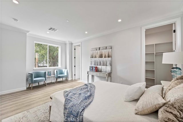 bedroom with crown molding, a walk in closet, and light hardwood / wood-style flooring