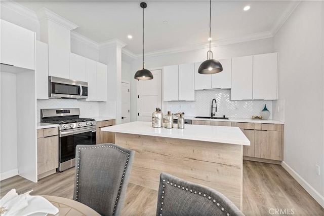 kitchen with sink, white cabinetry, ornamental molding, pendant lighting, and stainless steel appliances