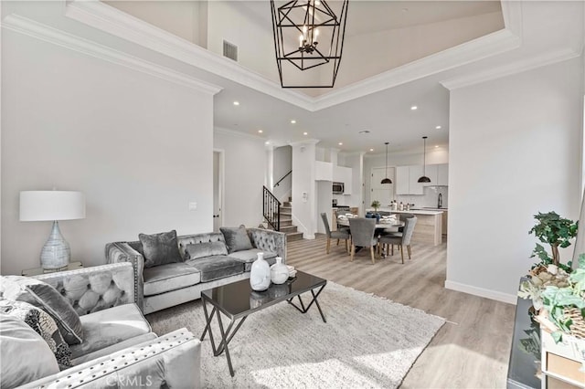 living room featuring crown molding, light hardwood / wood-style floors, a chandelier, and a towering ceiling