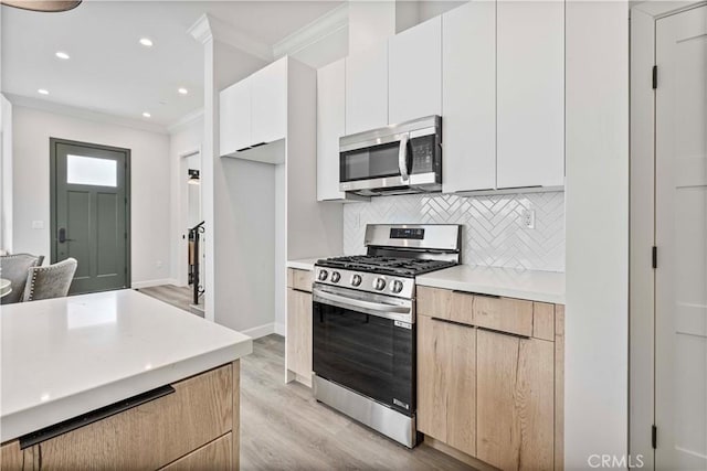 kitchen with tasteful backsplash, white cabinetry, ornamental molding, light hardwood / wood-style floors, and stainless steel appliances