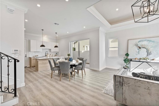 dining area featuring crown molding, sink, an inviting chandelier, and light hardwood / wood-style flooring